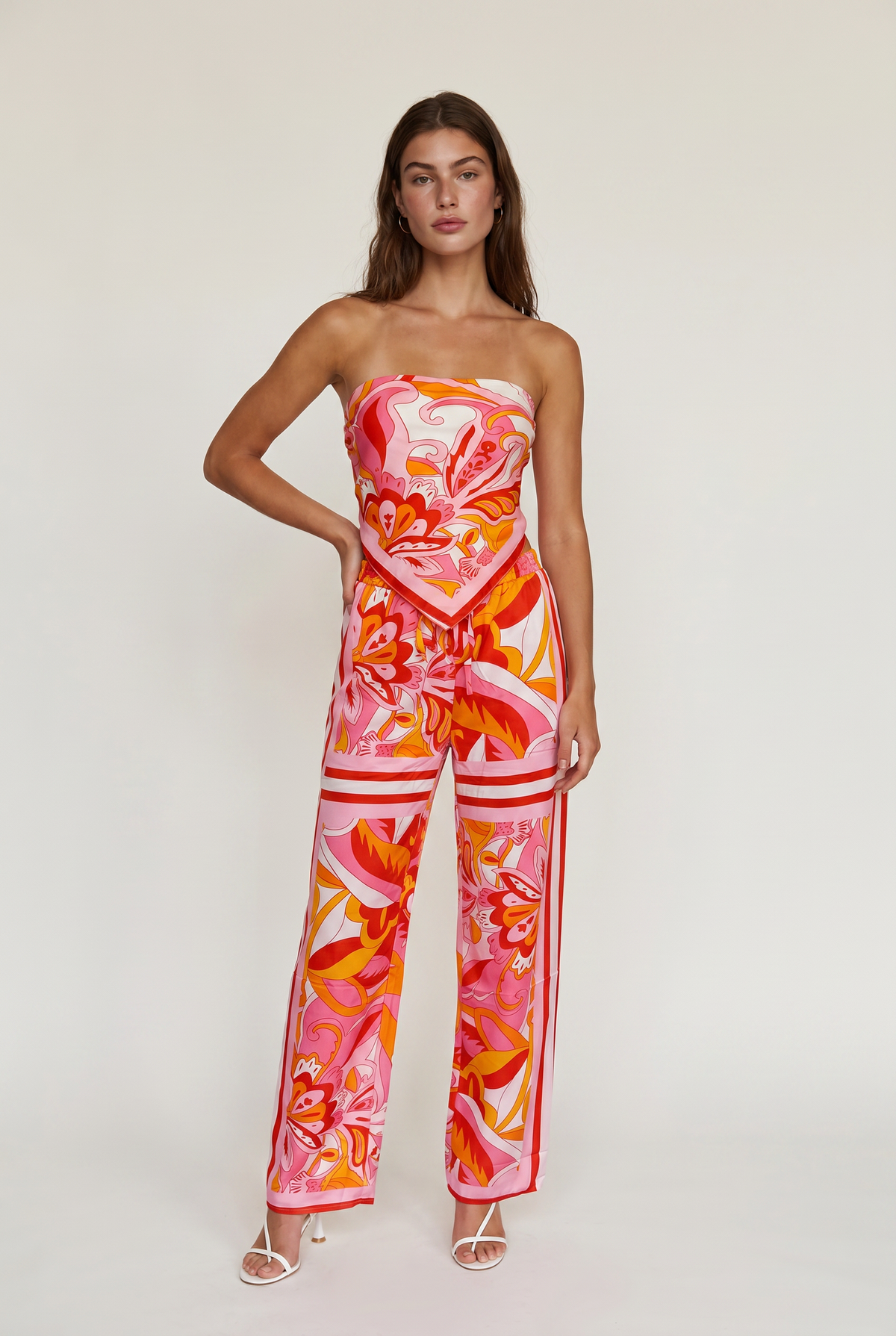 Image shoes a girl standing straight with her hand on hip wearing a printed strapless top and matching pants with white heels.