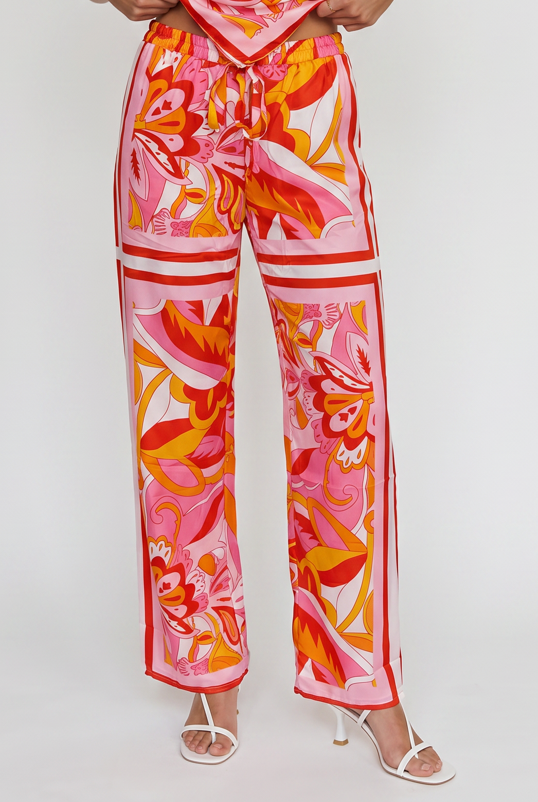 Image shoes a waist down image of the printed colored pants and white heels